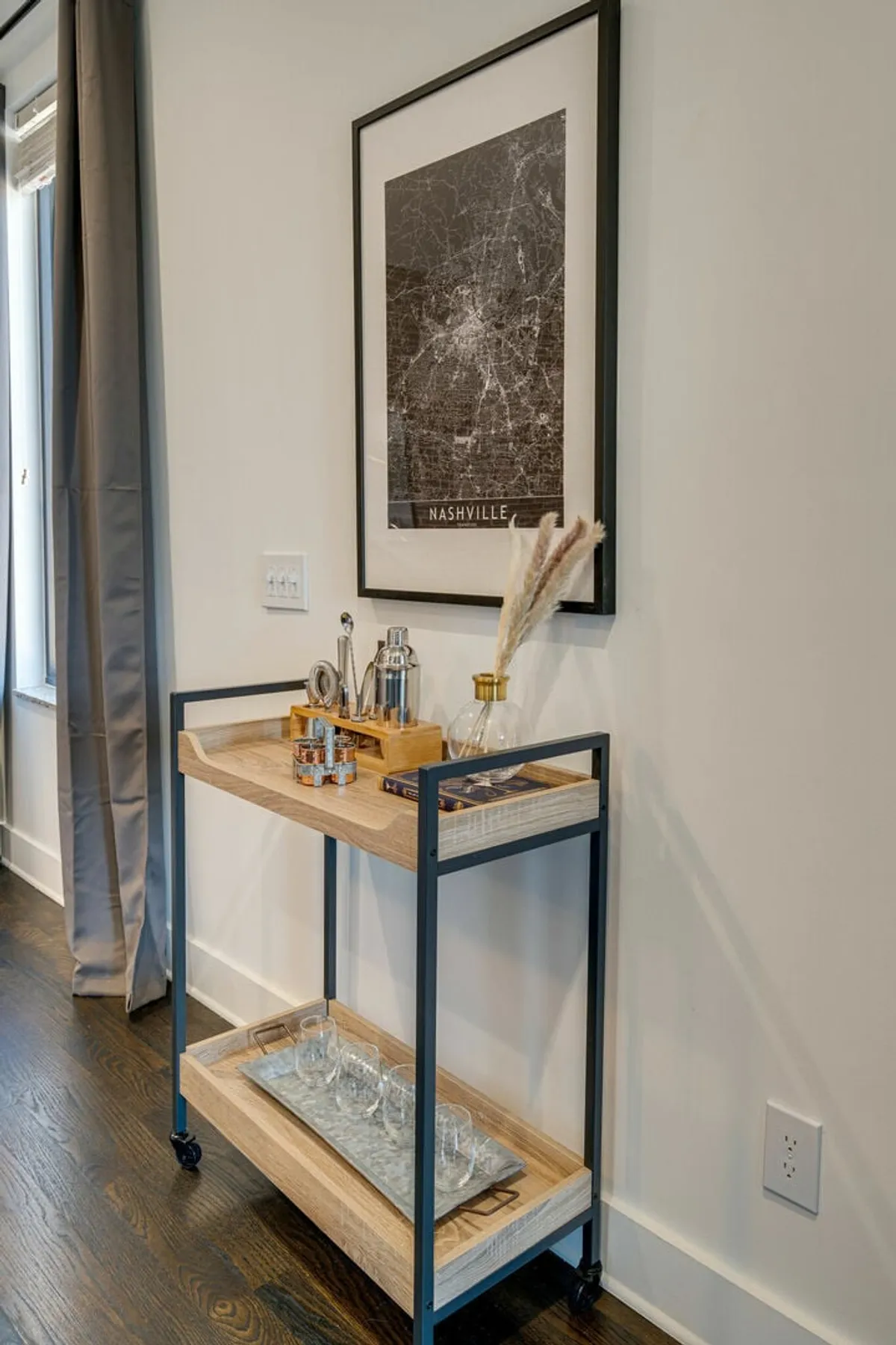 A sophisticated interior featuring a well-appointed bar cart, Nashville map artwork, and elegant glassware—suggesting both local flair and the comfort of entertaining guests in a private, upscale apartment setting.