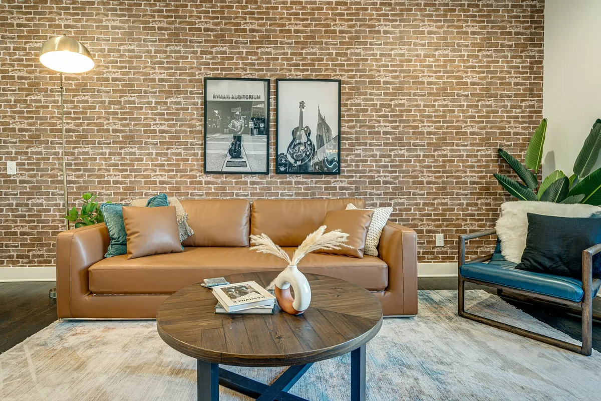 A chic interior featuring a leather sofa, a round wooden coffee table ready for board games or snacks, framed art on the wall, and a green plant adding freshness. The setup exudes approachability and is well-suited for entertaining or relaxing with friends.