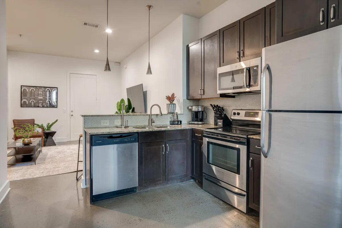 A bright, modern kitchen featuring a spacious island, stainless steel appliances, elegant pendant lighting, and decorative wall art. The kitchen is staged for both cooking and socializing, with ample counter space and contemporary finishes.