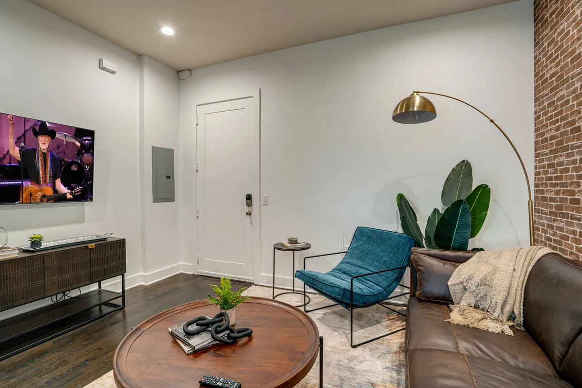 A welcoming living area with a large leather sofa, a round coffee table, an accent chair, a big green plant, and a television displaying a performance—suggesting space for movie nights or watching music events together.