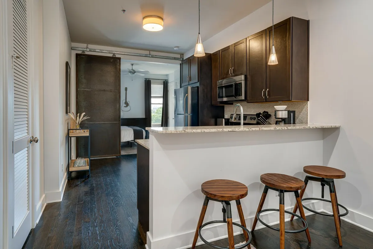 A contemporary kitchen with an island and bar stools, dark cabinetry, pendant lights, and an open layout that seamlessly connects to the living and dining areas. The design encourages both solo meal prep and group interaction.