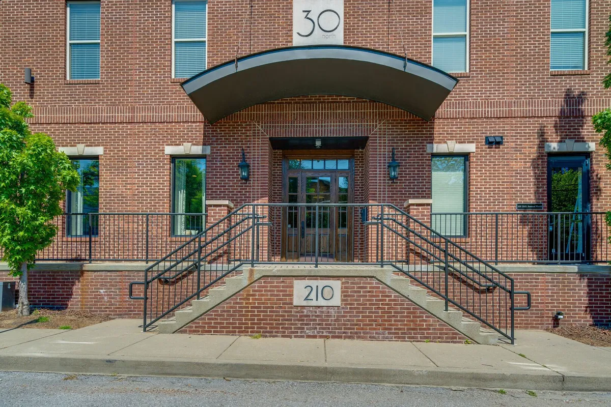 A welcoming exterior shot of an arched building entrance with a classic brick facade and a staircase leading up, set in a lively city neighborhood. The setting conveys both the security and the urban connectivity of the building.